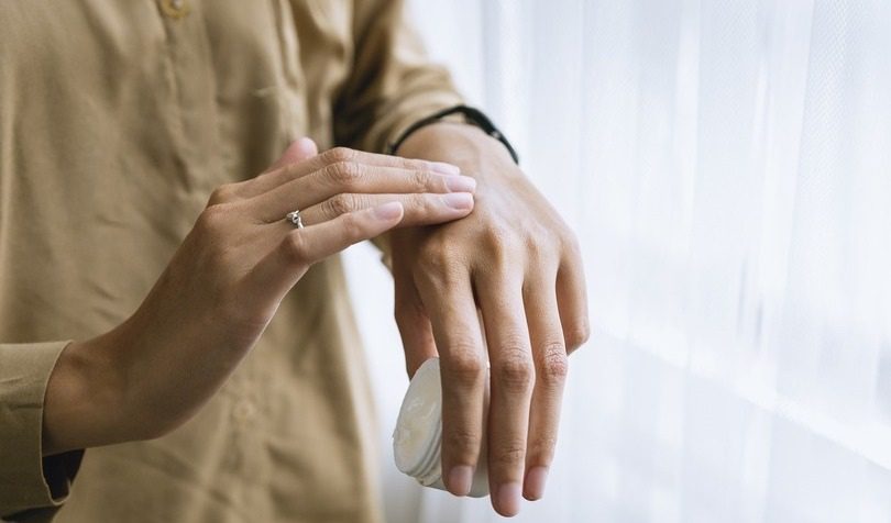 Žena u bež košulji nanosi kremu na ruku 