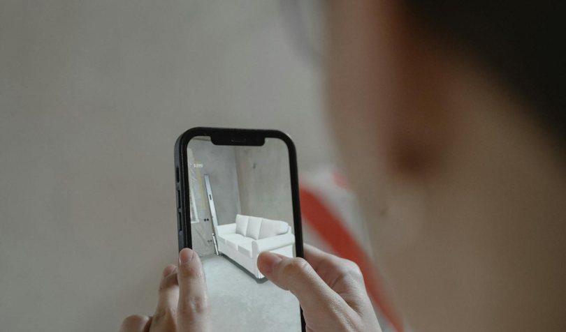 Osoba drži telefon na kojem je uključena kamera na kojoj se vidi beli kauč.