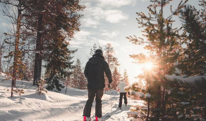 Dve osobe sa skijama na stazi okruženoj drvećem.