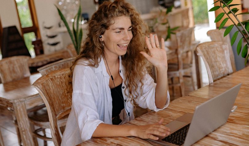 Žena u beloj košulji maše nekome preko web kamere na laptopu