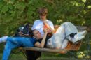 Dvoje mladih na drvenoj klupi, jedna osoba leži i pokazuje telefon drugoj
