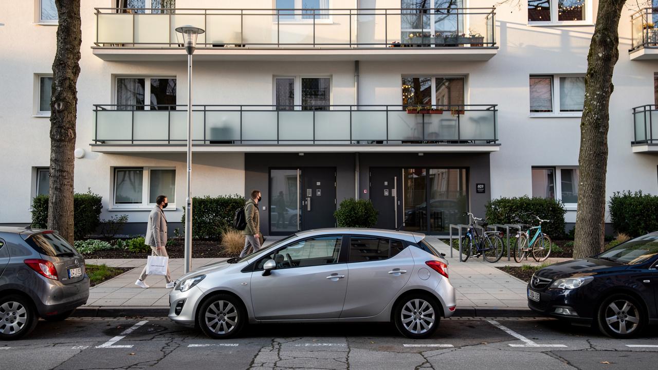 Sivi kompaktni automobil parkiran ispred stambene zgrade sa prolaznicima na trotoaru