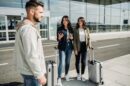 Dve žene sa koferima stoje ispred aerodroma i razgovaraju sa muškarcem